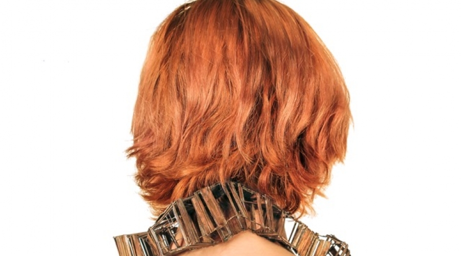 A rectangular necklace rests on the neck of a model with red hair 