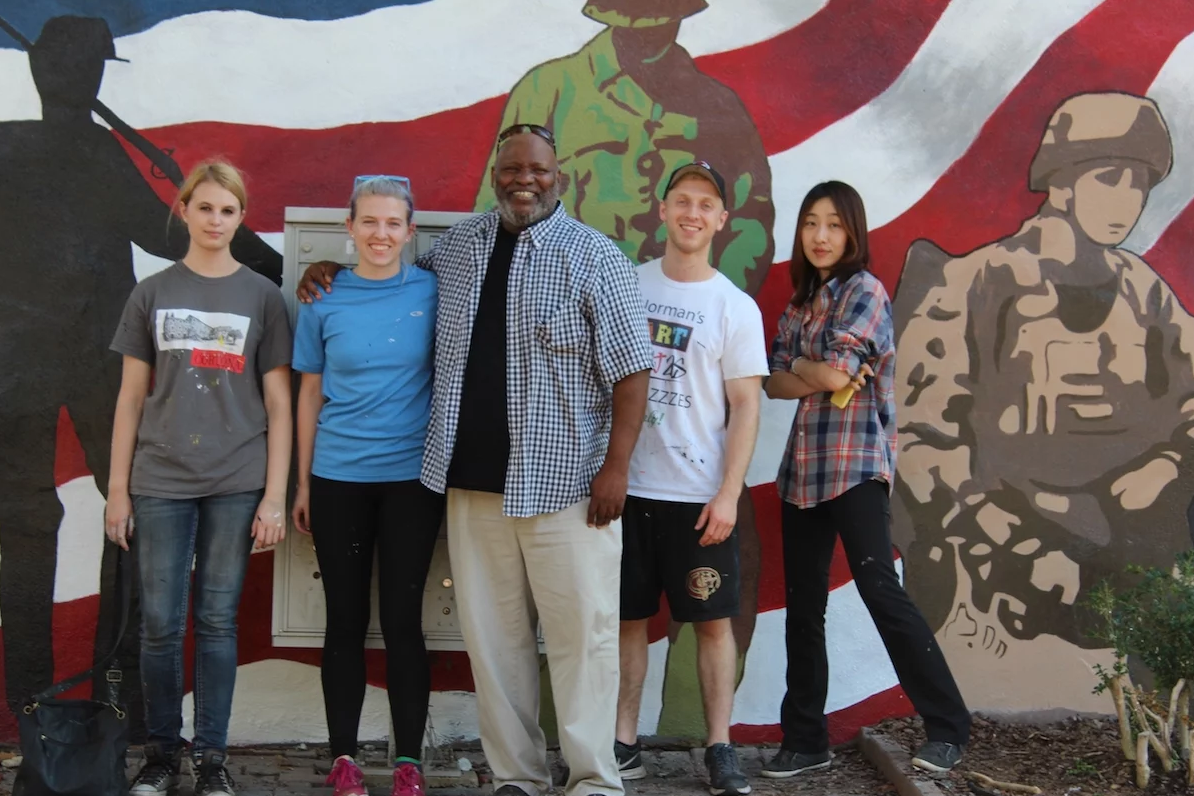Professor Joseph Norman (center) with students in front of a mural they created to honor veterans.