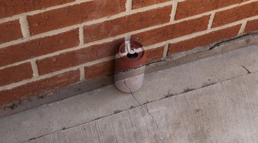 A can is painted to camouflage into a brick wall and sidewalk