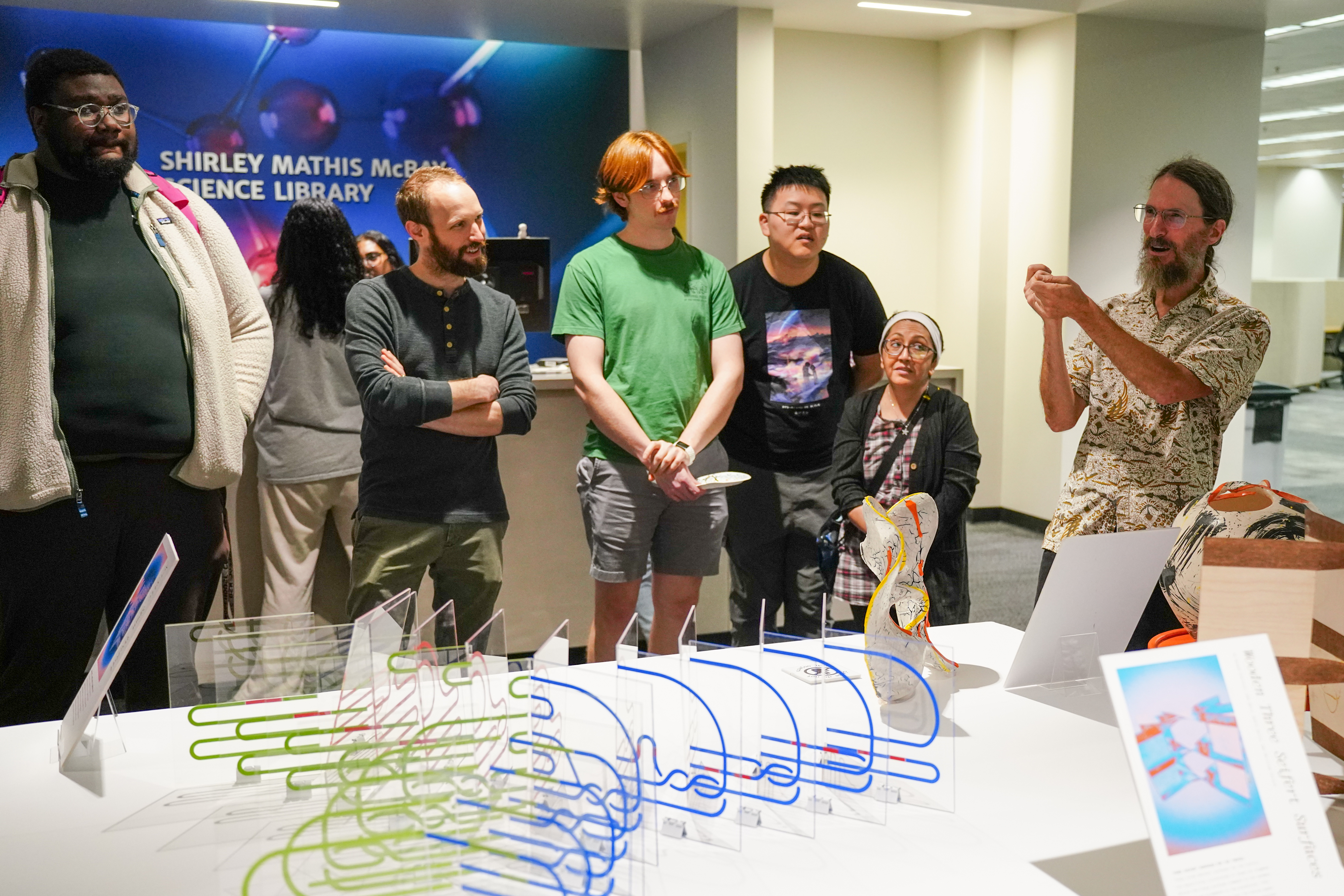 Professor Dave Gay discusses the Spacing Out exhibition during the opening, November 6, 2024. PhD student and exhibition organizer Alexander Tepper is shown second from the left. Photo courtesy of Sidney Chansamone.