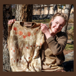 Individual outdoors smiling while holding up a brown dress with natural dyes