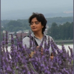 Person with short hair looking over their shoulder foregrounded by lavender flowers.