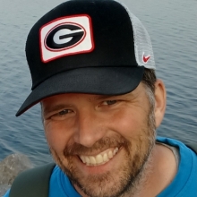 headshot of person smiling with beard and cap with University of Georgia logo.