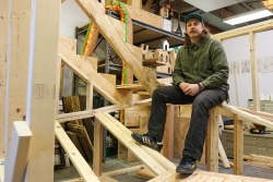 Mickey Boyd, '23 MFA, photographed sitting on the in-progress sculpture, Stairs and Portals to the Same Place, in his studio, February 3, 2023. Photo courtesy of Sidney Chansamone.