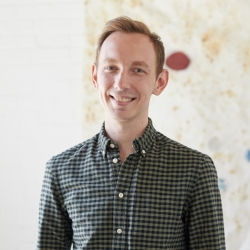 Person with short hair smiling in button-up shirt, indoors.