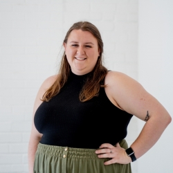 Person with long hair in black tank smiling with arm on hip, indoors.