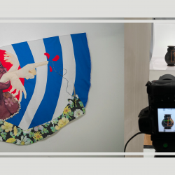 Image of mixed media artwork of person with mouth agape and arms extending out of mouth above red, blue, and white layered backdrop beside image of camera on tripod photographing a dark vase.