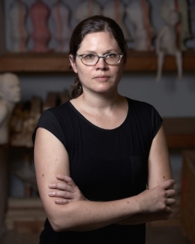 Headshot of Christina A. West. Person with glasses and black top with arms crossed indoors.
