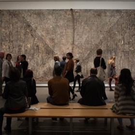 Interior gallery space with a crowd gathered in front of a large artwork on a white wall