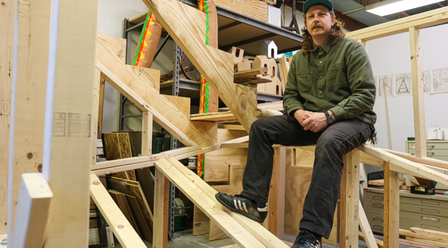 Mickey Boyd, '23 MFA, photographed sitting on the in-progress sculpture, Stairs and Portals to the Same Place, in his studio, February 3, 2023. Photo courtesy of Sidney Chansamone.