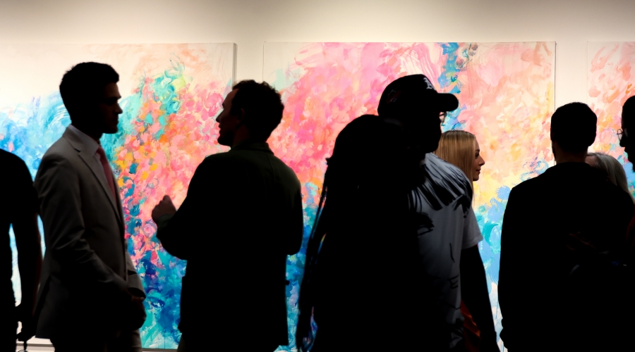 Group gathered indoors silhouetted against backdrop of pastel abstract paintings. Image courtesy of Sidney Chansamone