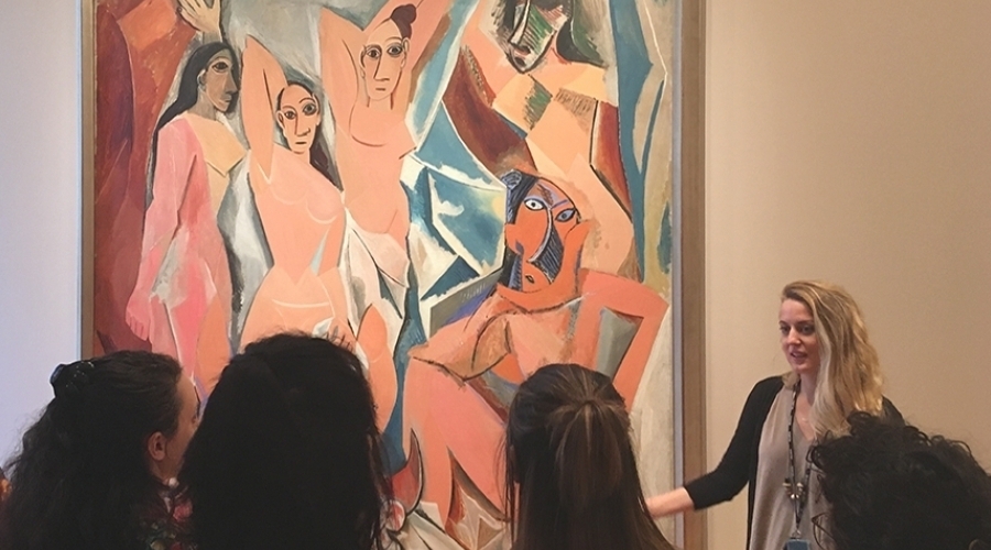 A woman stands in front of a painting in front of a group of people