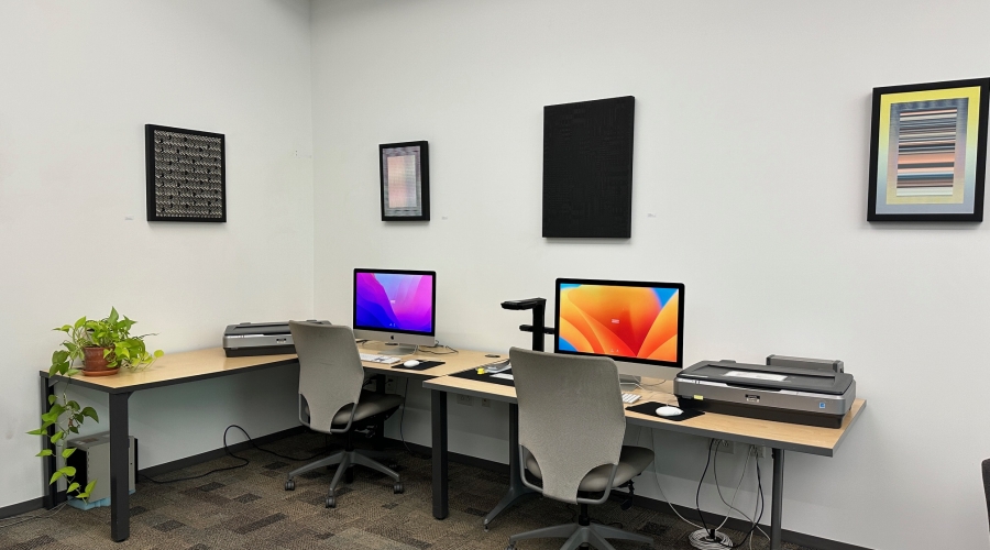 An image of the computer area. Two desktop computers are on top of tables. Both have flatbed scanners next to them. Between the two computers, there is an overhead scanner.