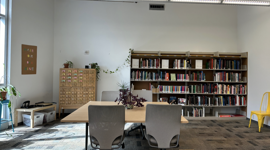 A view of the right or north side of the Art Library. Several shelves of books are lined against wall. Next to these shelves is a cabinet of drawers. Centered is a table with four chairs.