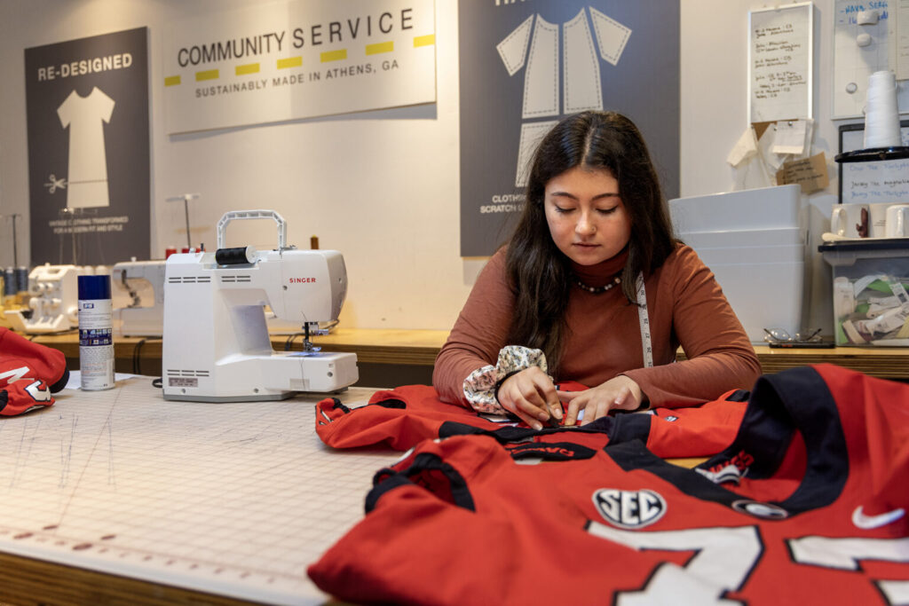 Lamar Dodd School of Art alumna and Community seamstress Julia Urrea (BFA in Fabric Design, '22) mends a football jersey at the Community Athens Boutique.
