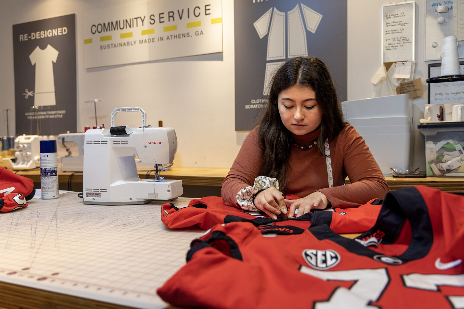 Lamar Dodd School of Art alumna and Community seamstress Julia Urrea (BFA in Fabric Design, '22) mends a football jersey at the Community Athens Boutique.