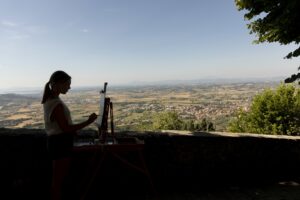 Undergraduate Karley Welch is silhouetted as she paints the Tuscany countryside along the wall below the John D. Kehoe Cortona Center.