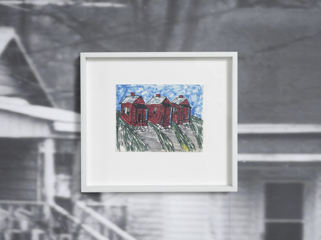 Installation view at the Athenaeum for “Beverly's Athens: Beverly Buchanan in Athens, GA”, Spring 2026. Framed drawing of three colorful red houses on with blue sky hung against detail of black and white photograph of houses. Photo courtesy of Walker Bankson.